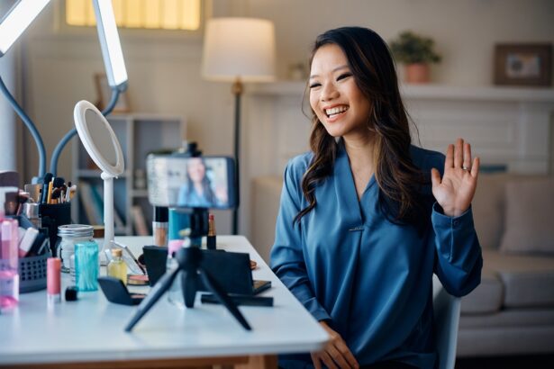 Happy Asian beauty influencer greeting her followers while recording makeup vlog at home.