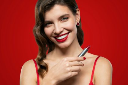 Portrait of elegant woman with red lips and evening makeup holding lipstick